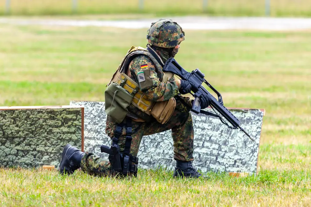 Kniender Bundeswehr-Soldat mit Gewehr und technischer Ausrüstung bei einer Übung während der militärischen Ausbildung.