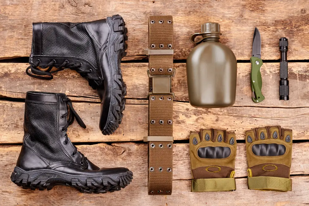 Militärstiefel und taktische Soldatenausrüstung der Bundeswehr mit Feldflasche und Handschuhen auf Holzgrund.