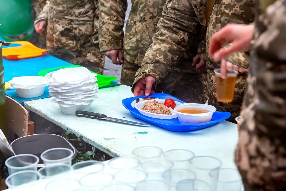 Soldaten in Uniform bei der Essensausgabe in einer militärischen Kantine oder Gemeinschaftsunterkunft.