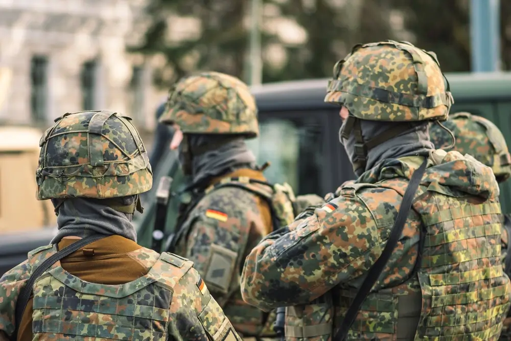 Rekruten der Bundeswehr in Uniform und mit Helmen bei der Ausbildung auf einem Übungsplatz.