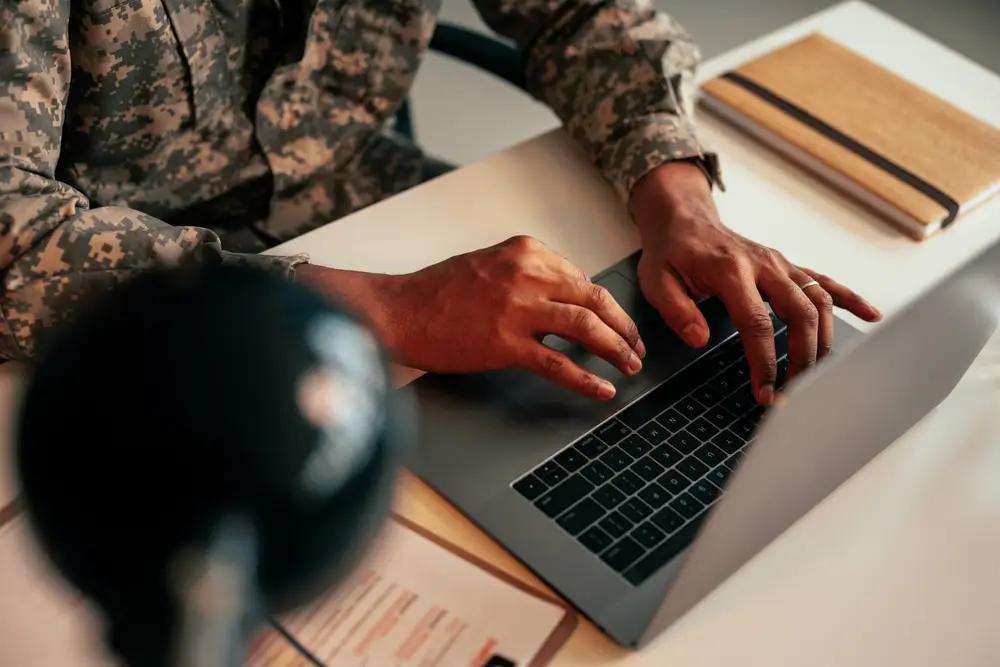 Ein Bundeswehr-Offizier in Uniform arbeitet am Laptop im Büro an administrativen Aufgaben im Stabsgebäude.