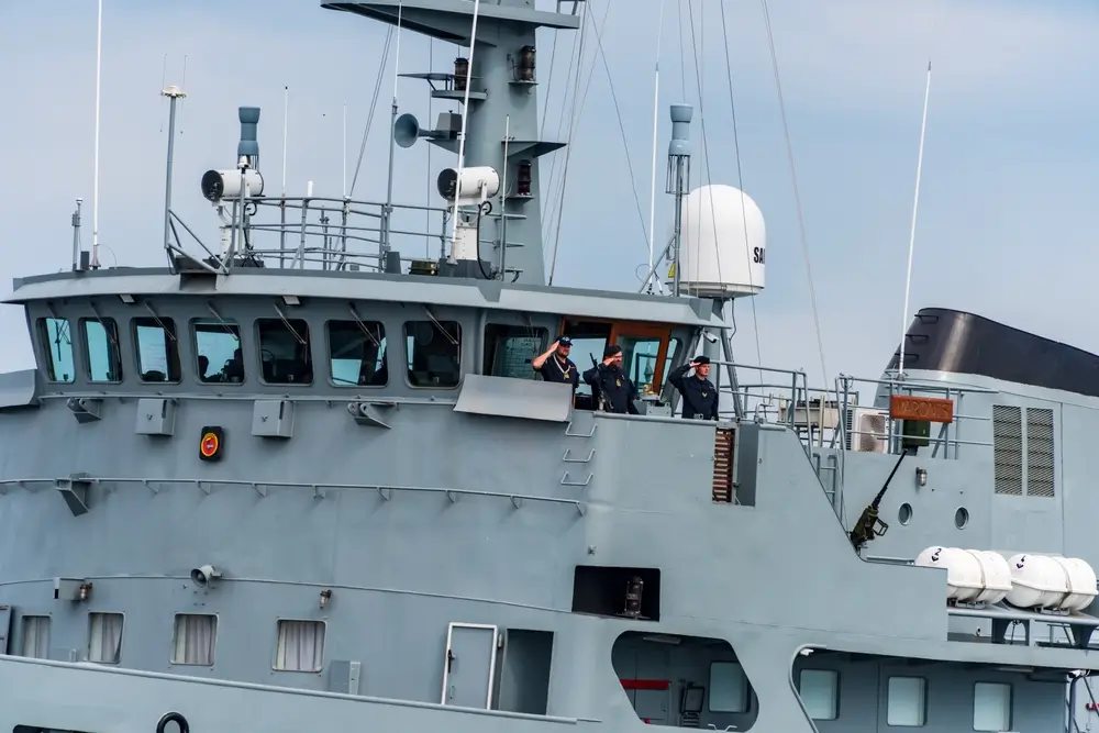 Drei Marineoffiziere salutieren auf der Brücke eines Schiffes der Deutschen Marine.