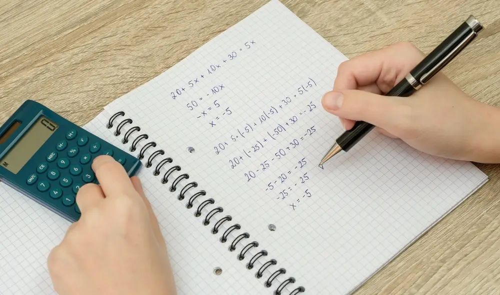 Hand löst eine Matheaufgabe mit Stift und Taschenrechner auf einem karierten Block zur Prüfungsvorbereitung.