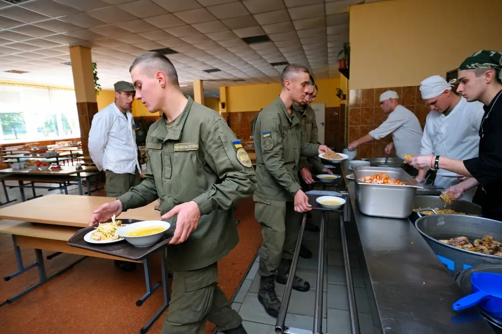 Soldaten in Uniform stehen an der Essensausgabe einer Truppenküche und nehmen ihre Verpflegung auf Tabletts entgegen.