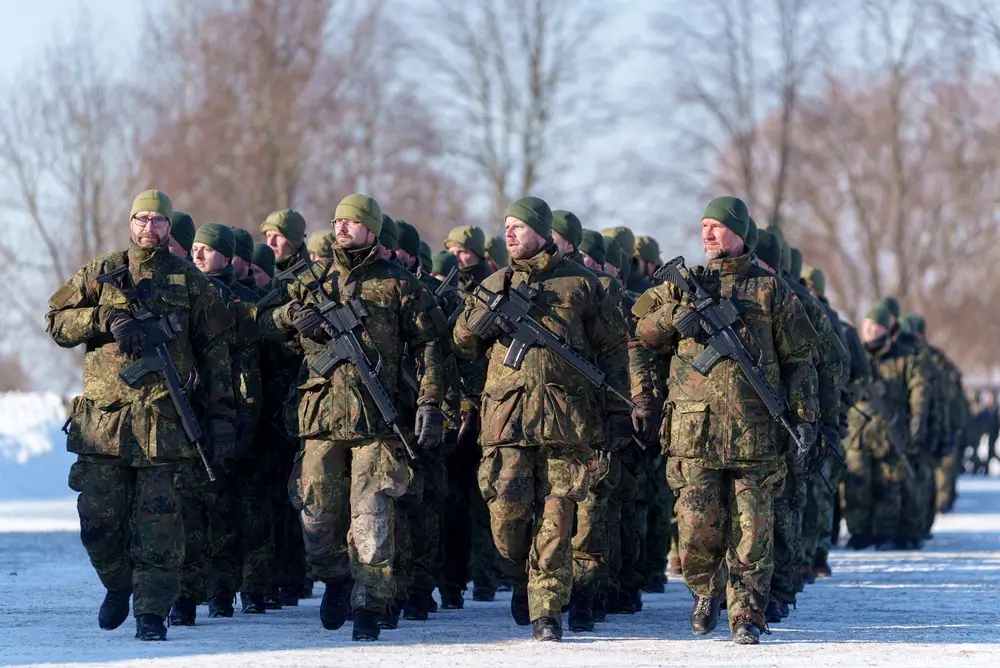 Bundeswehr-Soldaten marschieren in Uniform mit Gewehren im Schnee während ihrer militärischen Grundausbildung.
