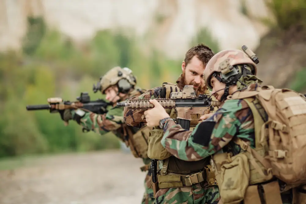 Feldwebel instruiert einen Soldaten bei einer Übung zur korrekten Handhabung der Waffe im Gelände.