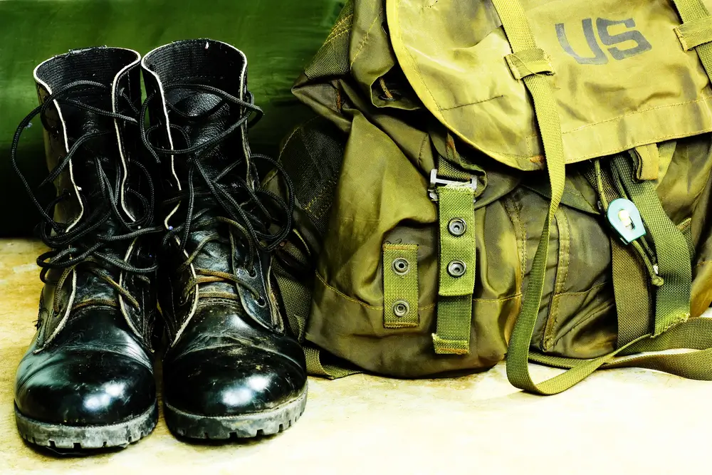 Schwarze Militärstiefel und olivgrüner Rucksack als Bundeswehr Ausrüstung für Soldaten in der Grundausbildung.