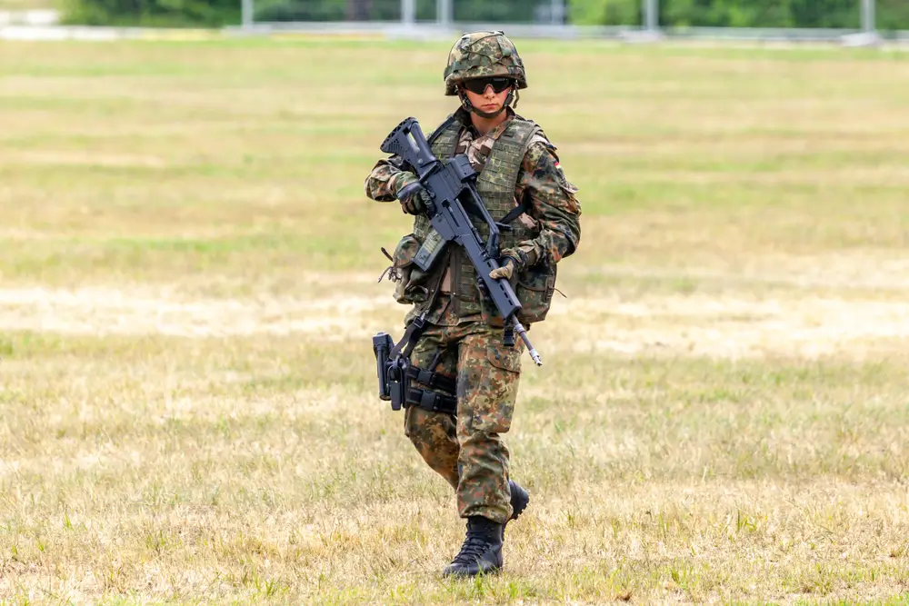 Bundeswehr-Soldat in Flecktarn mit Gewehr und Ausrüstung auf dem Übungsplatz während der Feldwebelausbildung.
