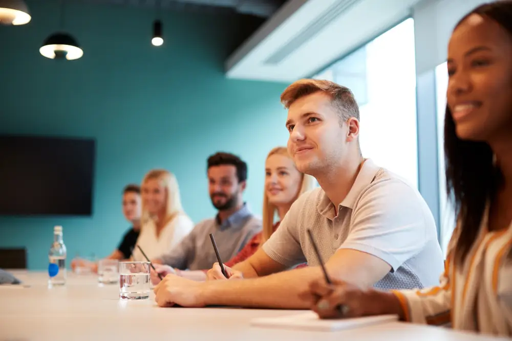 Junge Bewerber in einer Gruppe beim Einstellungstest im Assessment-Center konzentriert an einem langen Tisch.