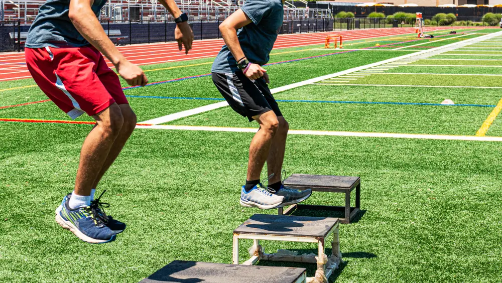 Zwei Männer beim Sprungtraining auf Boxen während des Bundeswehr Basis-Fitness-Tests auf einem Sportplatz.