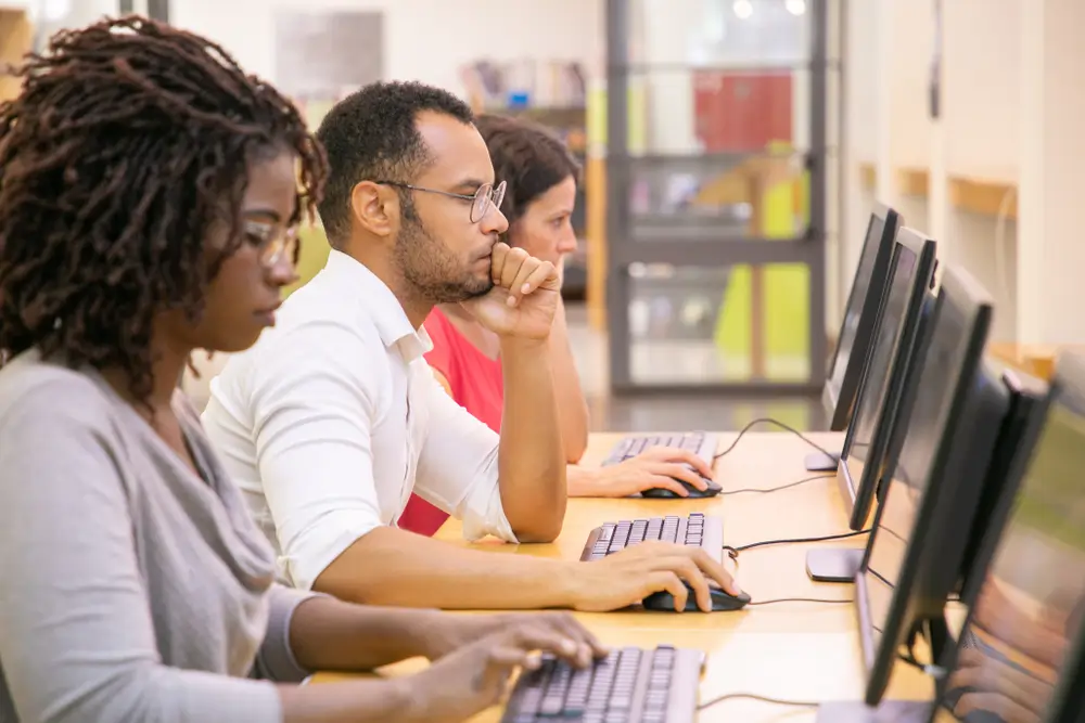 Konzentrierte Bewerber an Computer-Arbeitsplätzen während eines CAT-Einstellungstests in einem Testzentrum.