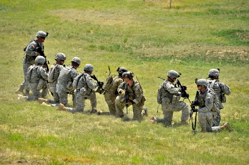 Infanteriesoldaten knien während einer militärischen Übung mit ihrer Ausrüstung in einem offenen Feld.