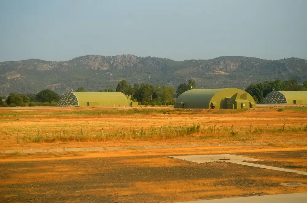 Grüne Militärgebäude und Hangars auf einem Kasernengelände der Bundeswehr vor einer Hügellandschaft.