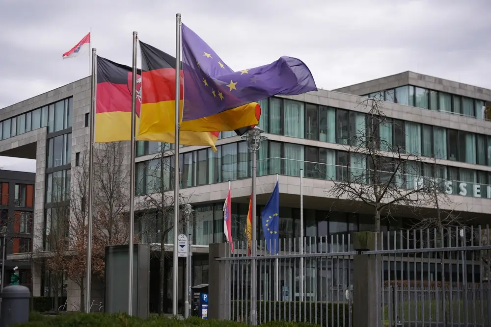 Modernes Bürogebäude der Bundeswehr-Verwaltung mit Deutschland- und EU-Flaggen vor einer hellen Fassade.