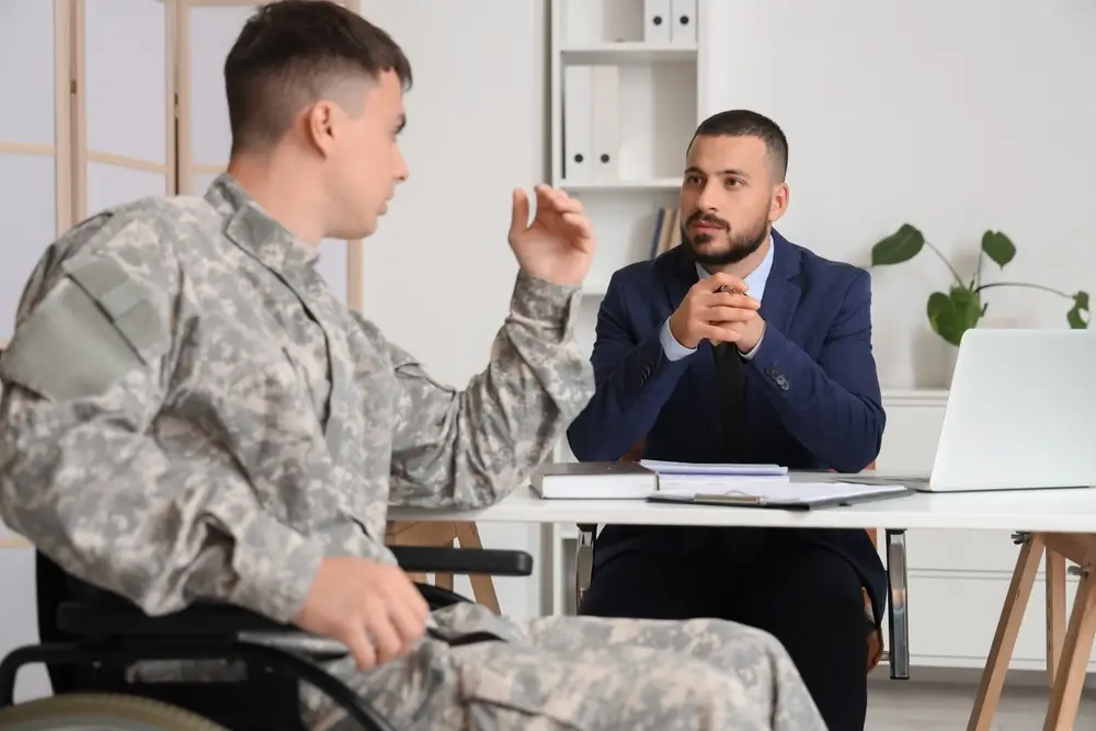 Soldat im Rollstuhl im Beratungsgespräch mit einem Karriereberater der Bundeswehr in einem hellen Büro.