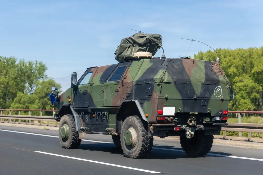 Gepanzertes militärisches Fahrzeug der Bundeswehr mit Tarnmuster fährt auf einer asphaltierten Straße vor Waldkulisse.