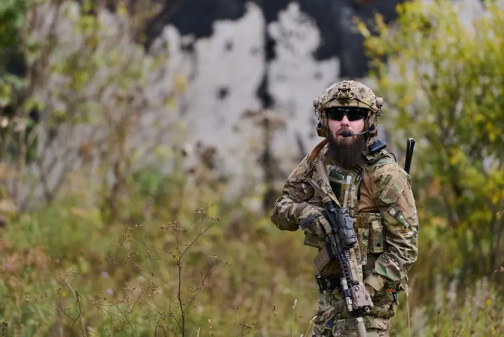 Soldat der Bundeswehr bei einer Patrouillenübung im Gelände mit voller Ausrüstung und Gewehr zur Positionssicherung.