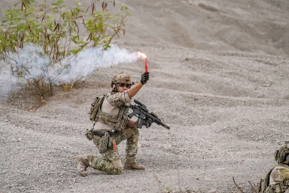 Soldatin in Einsatzkleidung kniet bei einer Bundeswehr-Übung im Gelände und hält ein brennendes Signallicht hoch.