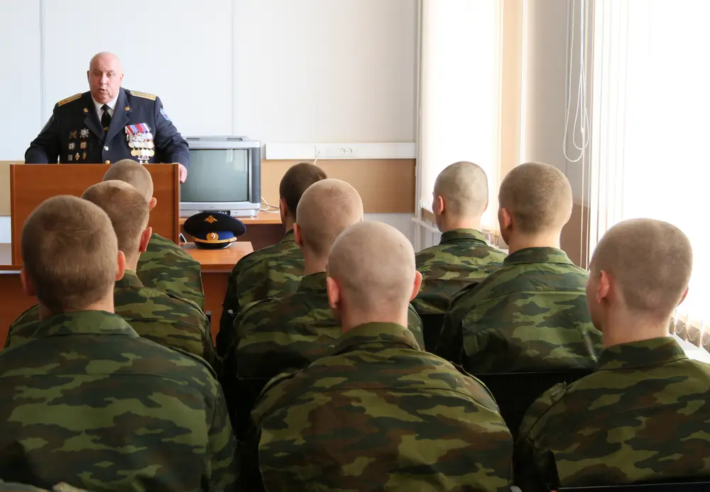 Ein Offizier hält eine Ansprache vor Soldaten in Uniform während einer militärischen Besprechung im Stabsgebäude.